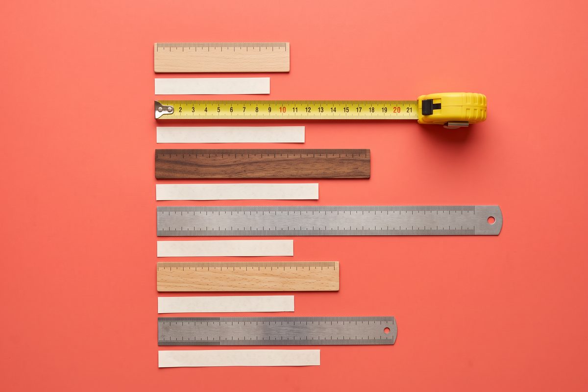 Flat-lay of rulers and paper strips cut to different lengths on a coral background.