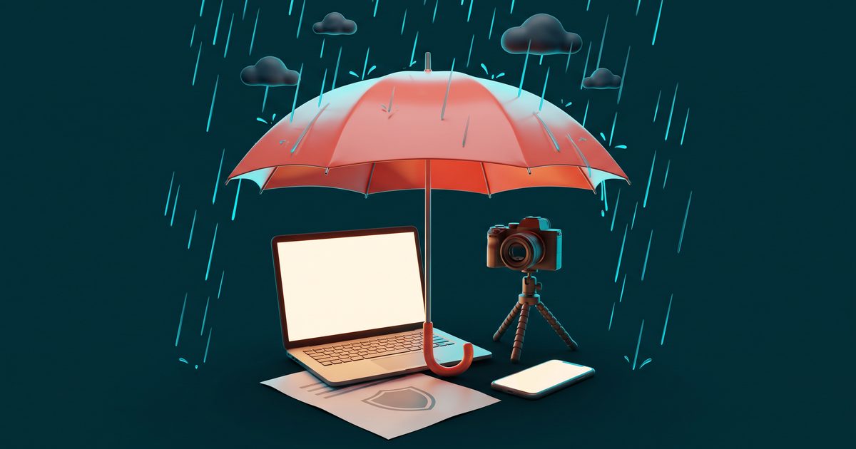 A large red umbrella shielding a laptop, a camera on a tripod and a smartphone from rain.