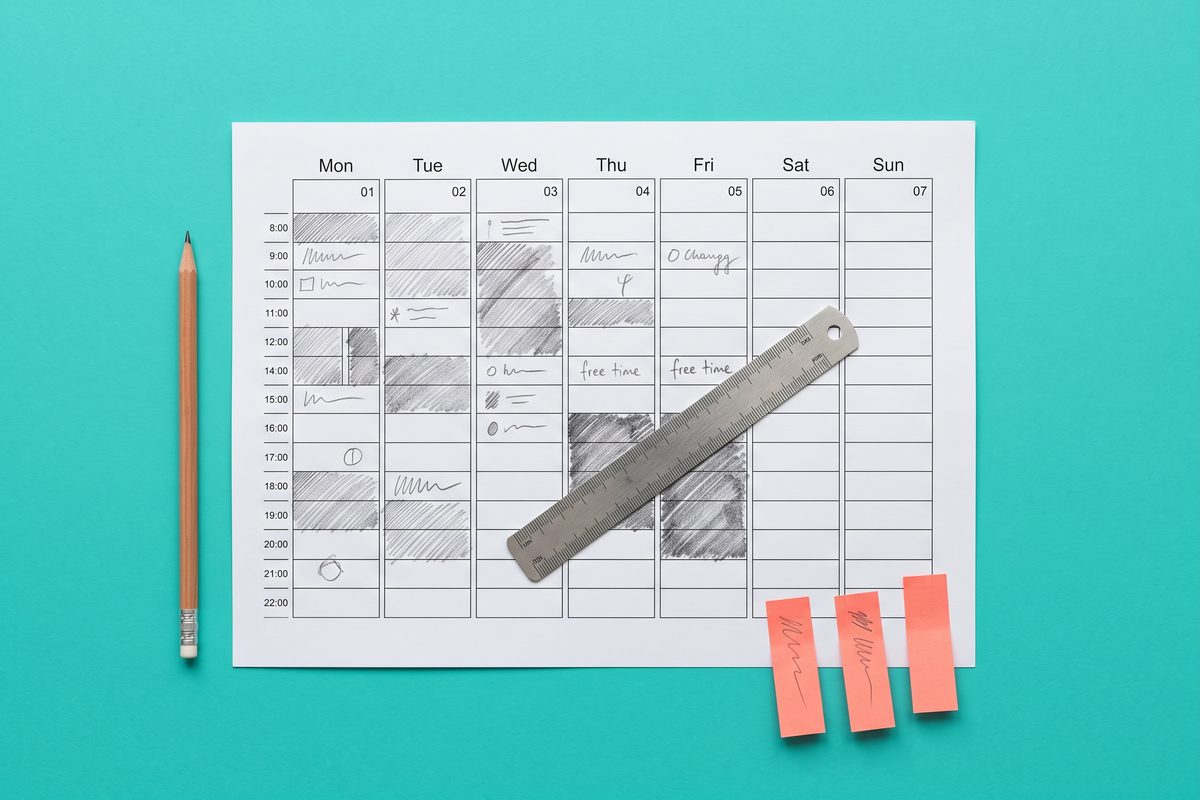 Overhead view of a printed week calendar on teal, with three coral sticky notes set aside and a ruler across it.