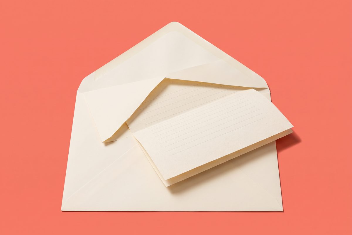 Oversized cream envelope with a folded blank letter halfway out on a plain coral background