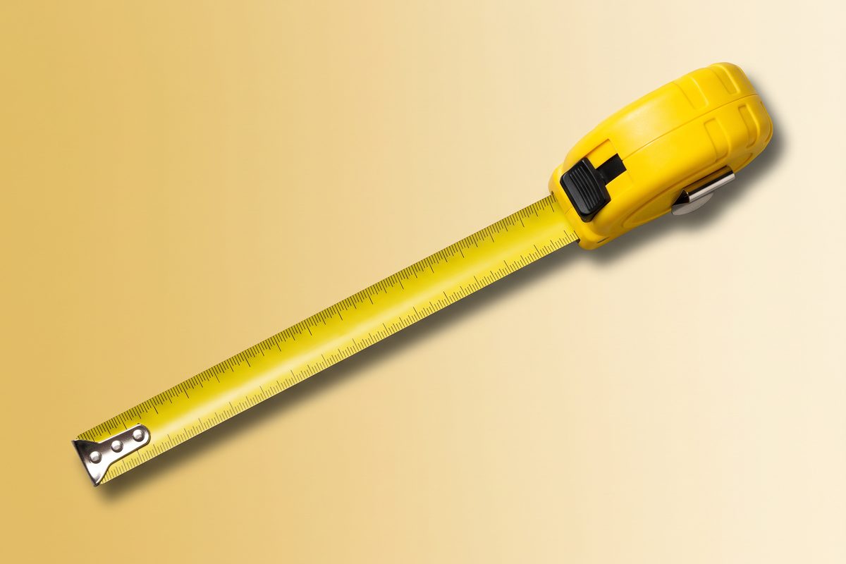 Oversized yellow tape measure lying diagonally on a plain cream background