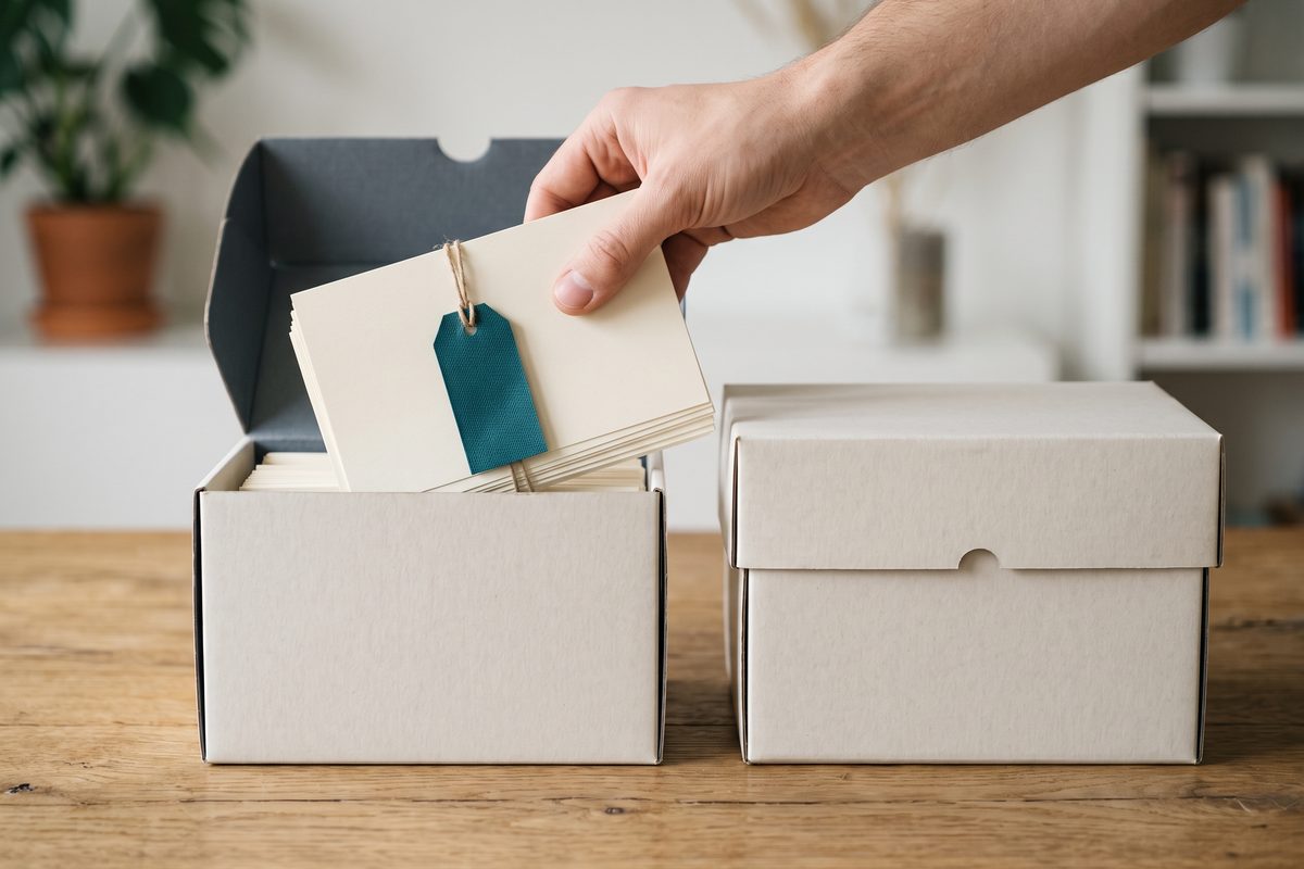 Index cards being moved from one archive box to another on a wooden desk