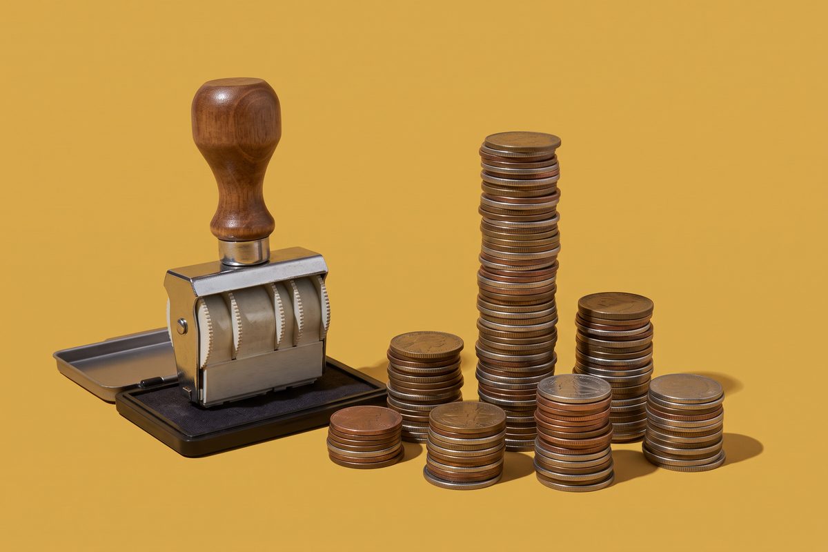 An oversized rubber stamp beside seven uneven stacks of coins, one far taller than the others.