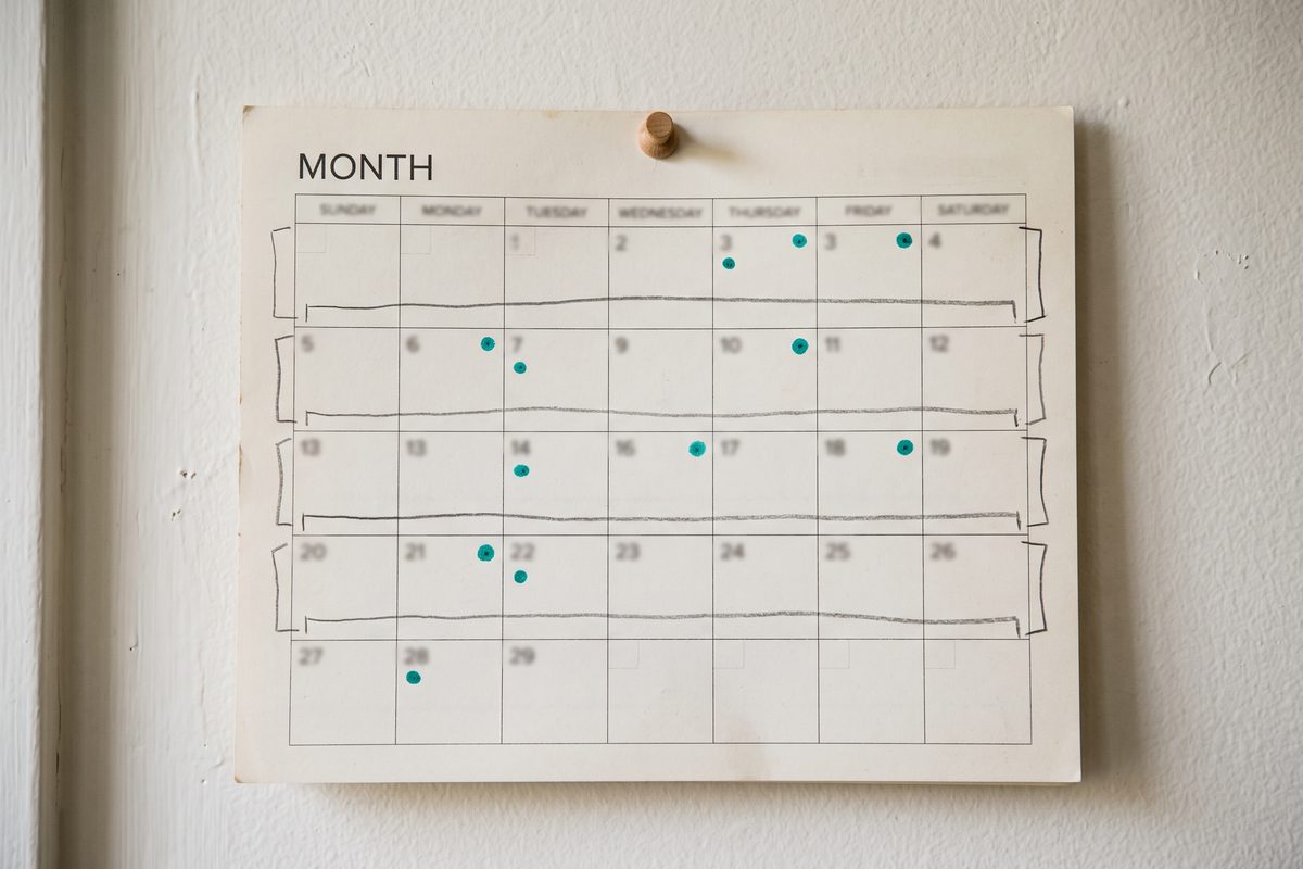 Paper wall calendar with four pencil brackets across the weeks and four small teal dots marking checkpoint days