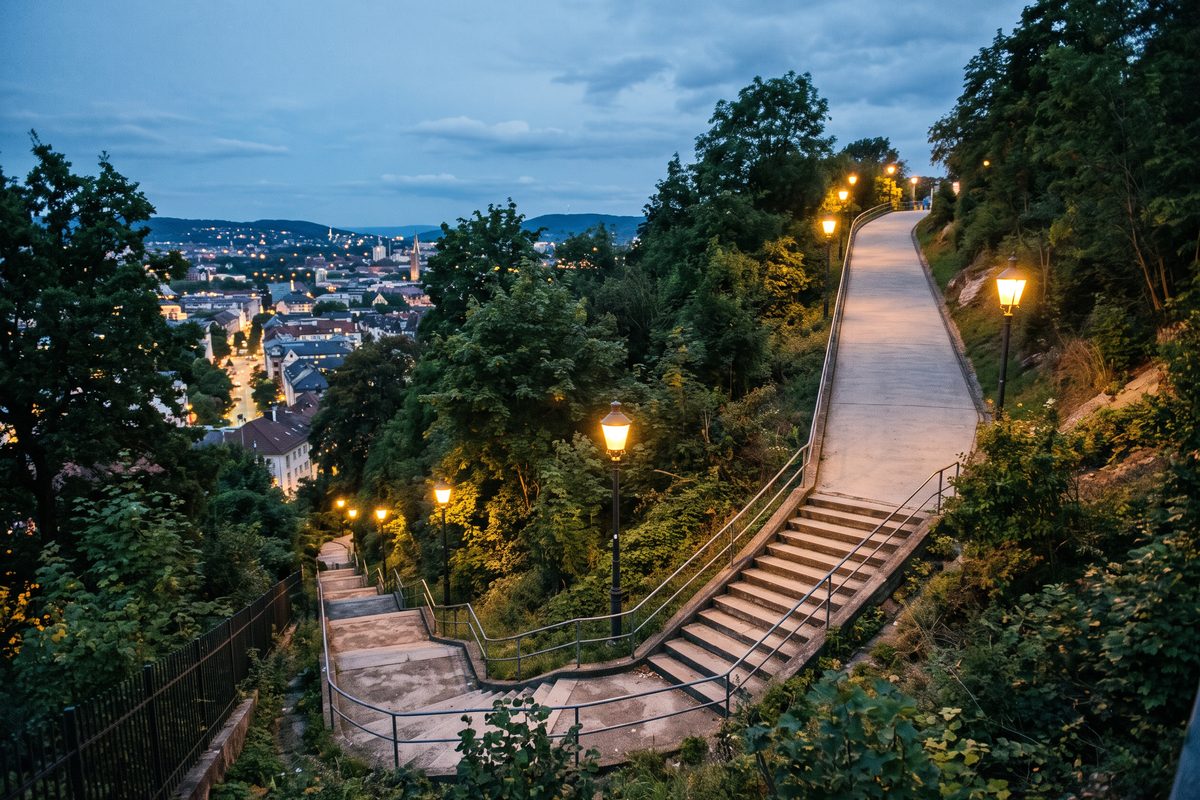 Outdoor staircase at dusk that climbs steeply and then flattens into a gentle ramp near the top.
