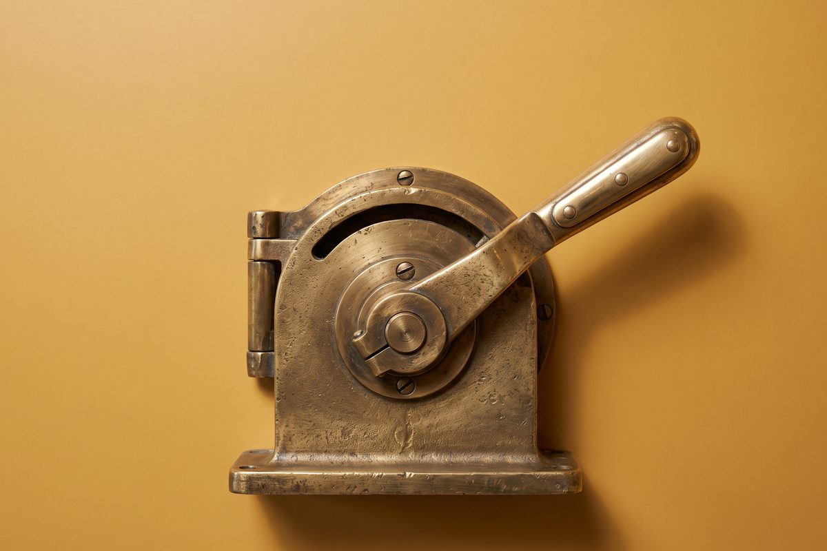 A single oversized brass lever on a plain mustard background, half pulled.