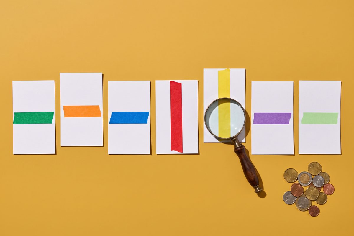 Seven blank cards with different-length tape strips and a magnifying glass on a mustard background.